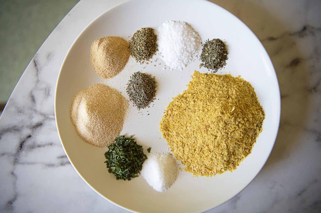 All of the separate ingredients that make up a chicken bouillon powder on a white plate.