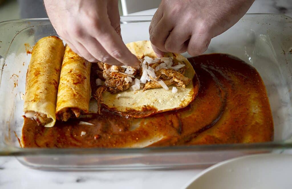 hands wrap an enchilada in a red sauce