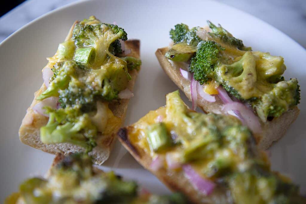 Four broccoli melts on a white plate - broccoli melt recipe