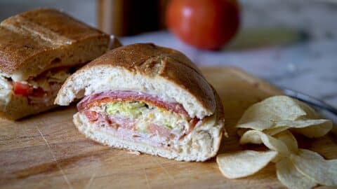 a grinder sandwich split in half next to potato chips.