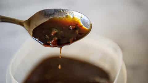 A dark Sweet soy glaze drips off the end of a spoon.