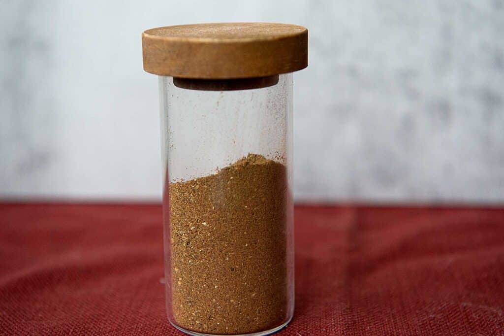 A dark brown blend of spices in a small container.