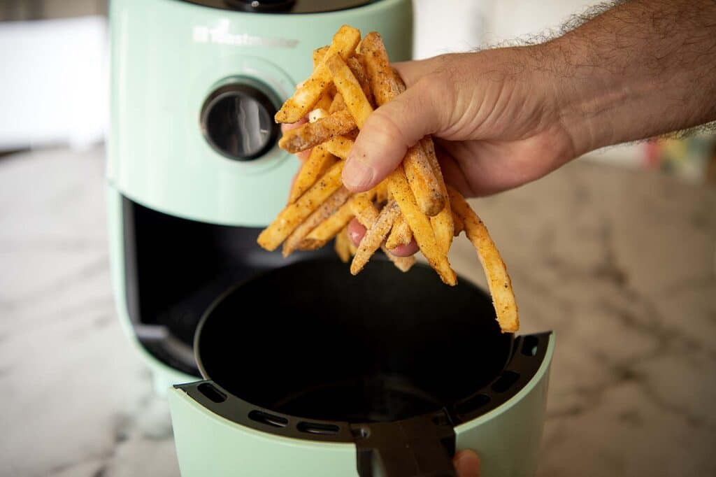 A hand placing checkers fries in an air fryer.