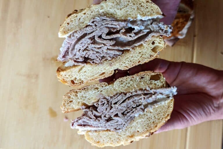 A beef on weck split in two and being shown in a manner that allows you to see the inside of the sandwich.