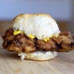 A crispy chicken biscuit sandwich with mustard sits on a wooden surface, showcasing a golden, flaky biscuit and crunchy chicken fillet in this classic chicken biscuit delight.