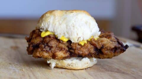 A crispy chicken biscuit sandwich with mustard sits on a wooden surface, showcasing a golden, flaky biscuit and crunchy chicken fillet in this classic chicken biscuit delight.