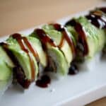 Very nice up close shot of eel sauce drizzled over avocado on top of a maki roll.