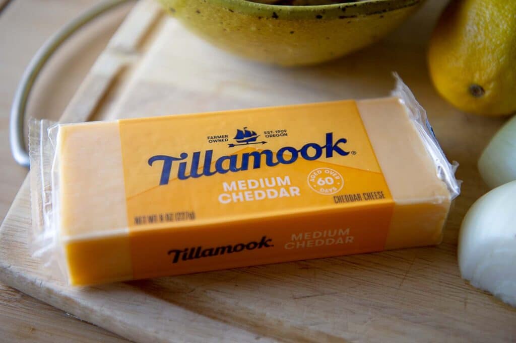 A block of Tillamook medium cheddar cheese on a cutting board.