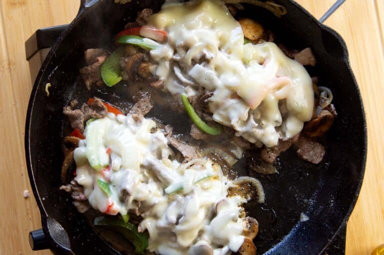 Top view shot of the ingredients of a steak bomb coming together in a cast iron pan.