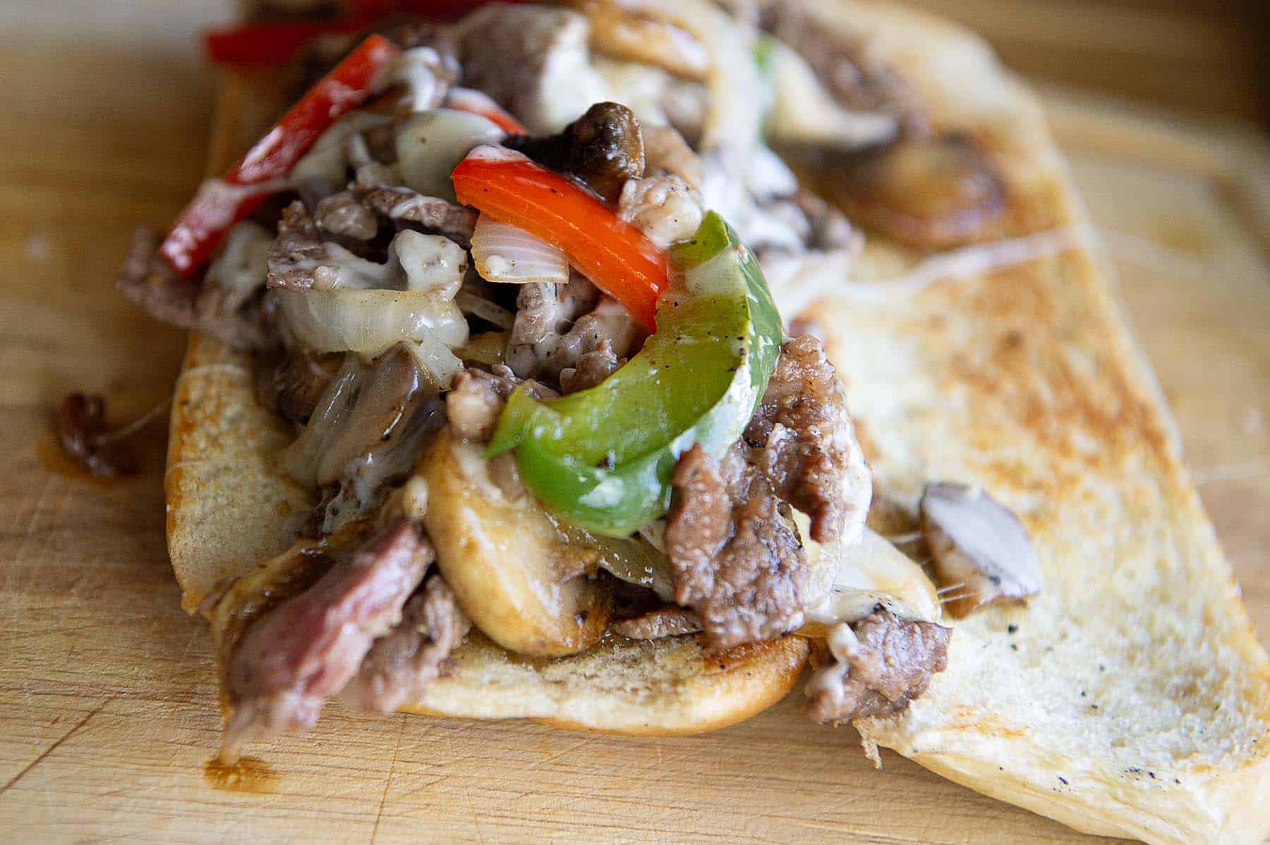 A steak bomb sandwich that is open face where you can see all of the ingredients.