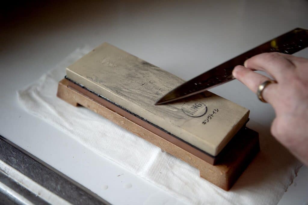 A photo showing a Chef sharpening their knife by using a double sided whetstone.