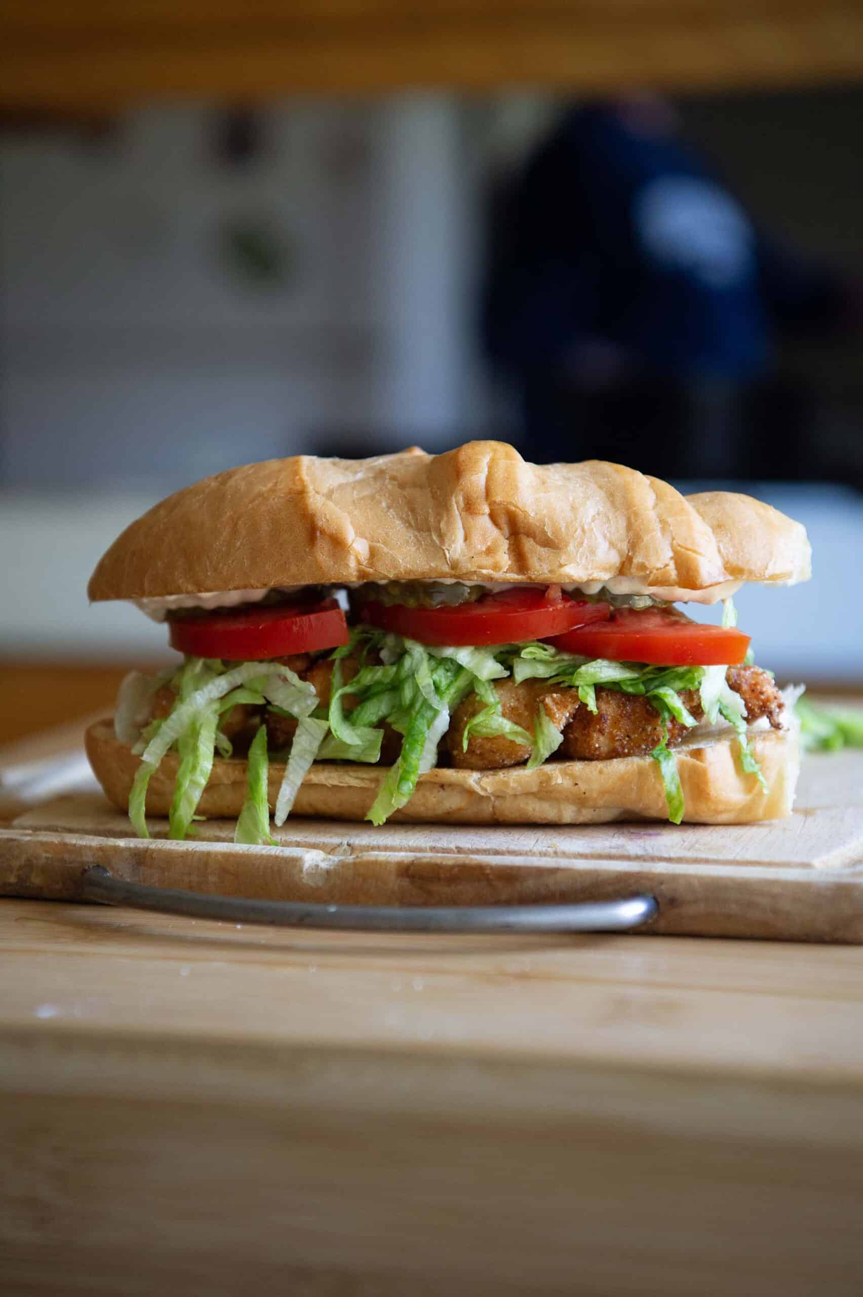 A shrimp po boy sitting on a wooden cutting board.