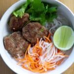 A close up of bun cha in a bowl. You can see shredded carrots, daikon, lime, and cilantro in the same bowl.