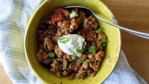 Turkey chili sitting in a yellow bowl with a dallop of sour cream in the middle. There is also a spoon in the chili.