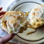 A picture showing the Chef picking up a cinnamon roll from a plate.