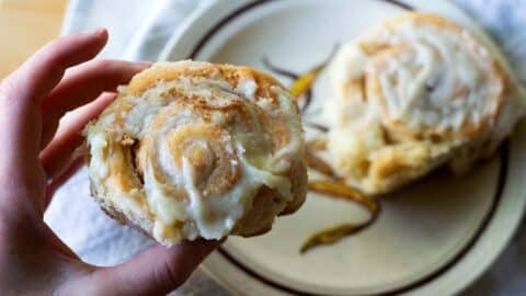 A picture showing the Chef picking up a cinnamon roll from a plate.