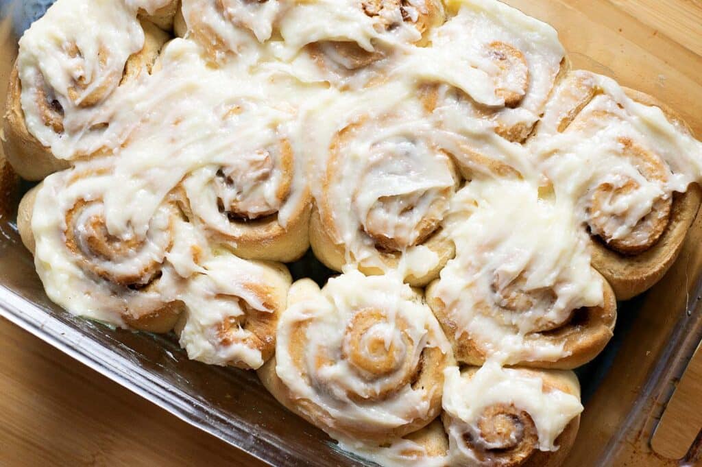 Cinnamon rolls in a glass pan with glaze over the top of them.