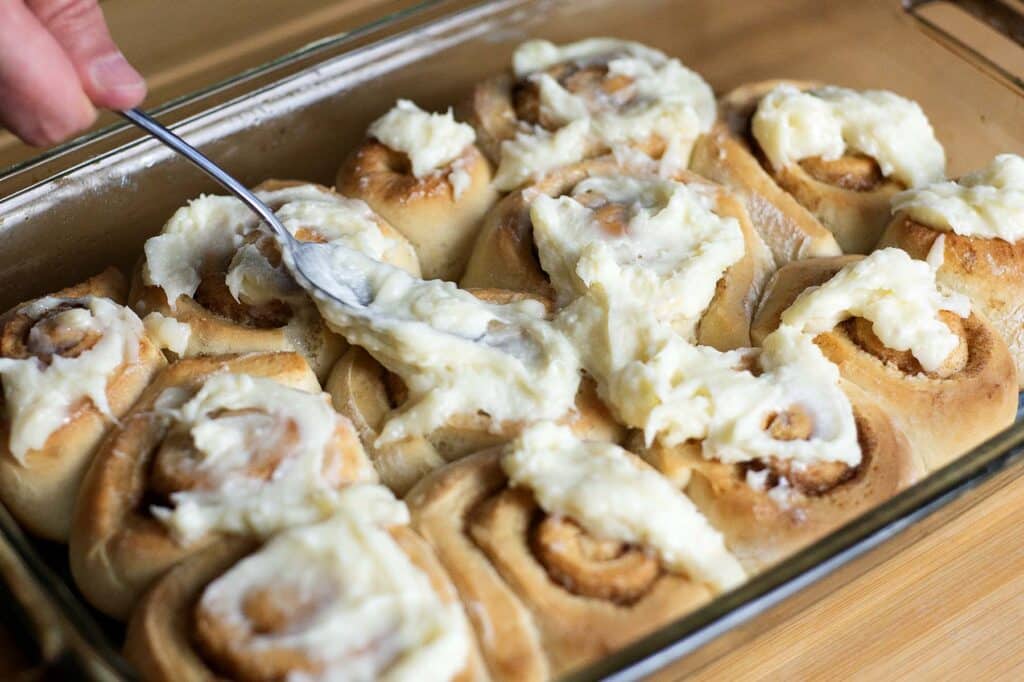 All of the cinnamon rolls being covered with the glaze after coming out of the oven.