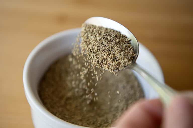 Ajwain being poured into a ramakin via a spoon.