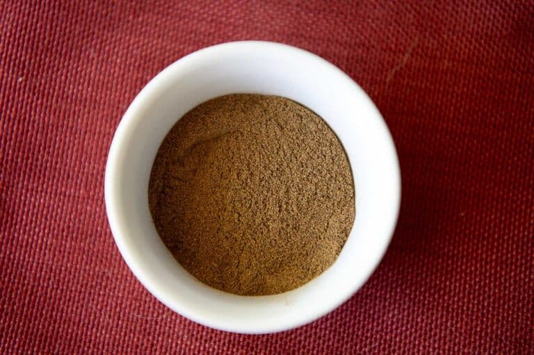 The spice blend known as allspice in a container with a red fabric backdrop.