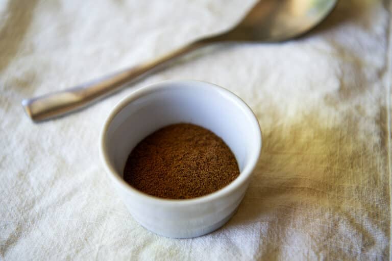 Allspice in a container with a spoon in the background.