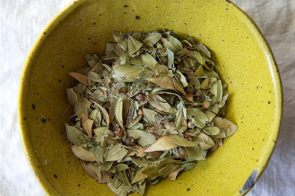 Top down shot of myrtle leaves resting in a yellow bowl.
