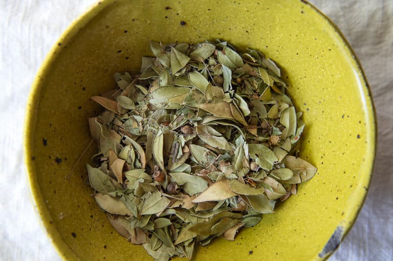 Top down shot of myrtle leaves resting in a yellow bowl.