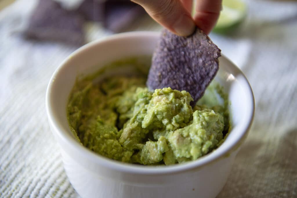 A blue corn tortilla chip being dipped into a 4 ingredient guacamole.