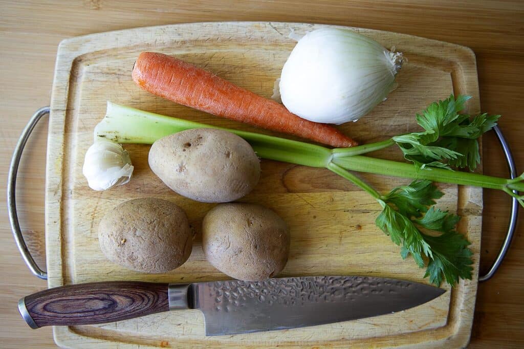 A picture showing an onion , garlic, celery, carrot, and potatoes for Knoephla soup.