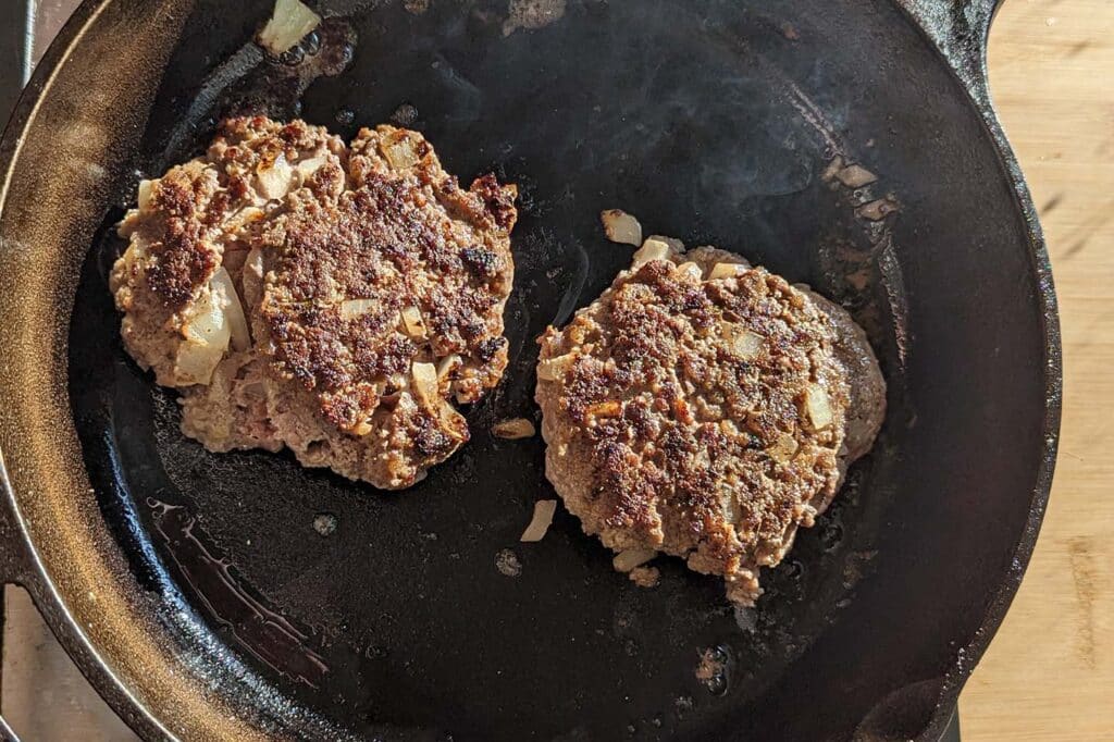 beef patties cooking on a cast iron skillet