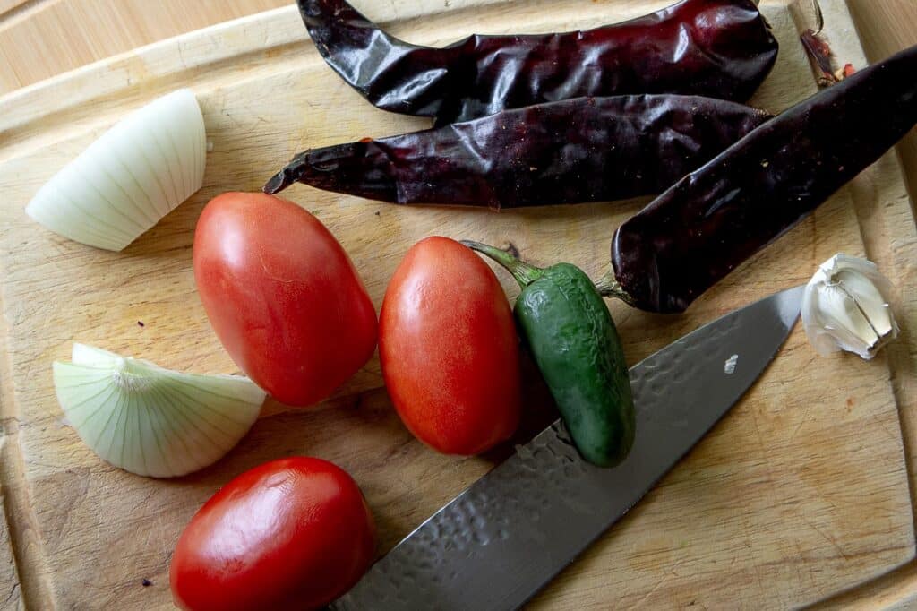 We see tomatos, peppers, garlic, and lime for the start of a sauce for Migas.