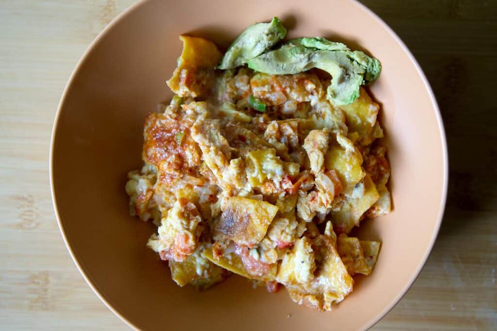 Top down shot of a bowl full of finished migas with avocado on the side.