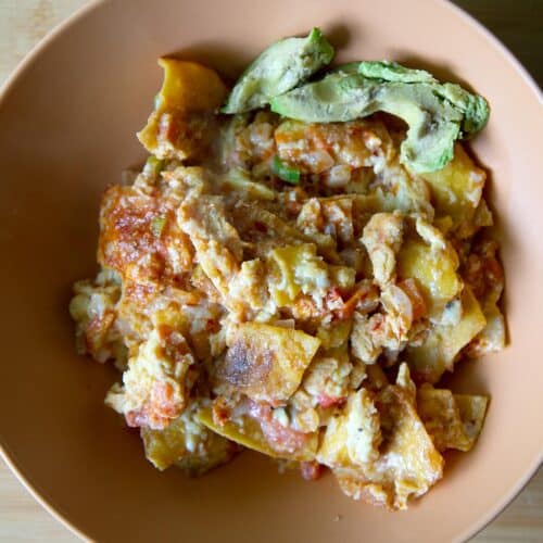 Top down shot of a bowl full of finished migas with avocado on the side.