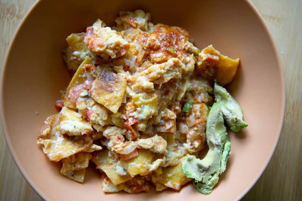 Top down shot of a bowl full of finished migas with avocado on the side.