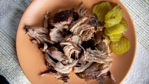 smoked pork butt on a ceramic plate with pickles on the side.