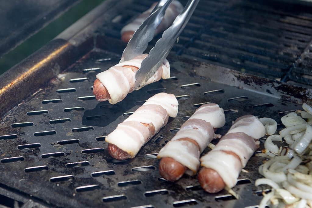 All beef hot dogs wrapped in bacon on a grill.