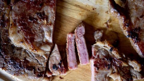 Pieces of a steak sitting on a cutting board after being cooked.
