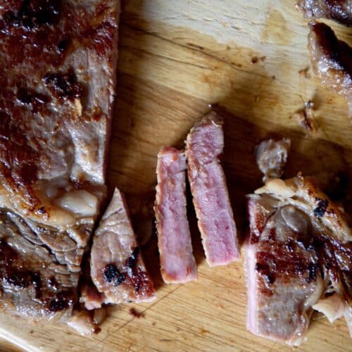 Pieces of a steak sitting on a cutting board after being cooked.