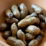 A close-up of a bowl filled with boiled peanuts, showing their slightly wrinkled shells and moist texture inside a brown dish. The boiled peanuts glisten softly, highlighting their fresh, savory appeal.