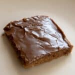 A single square piece of Texas Sheet Cake brownie with a cracked, shiny top sits on a plain white plate.