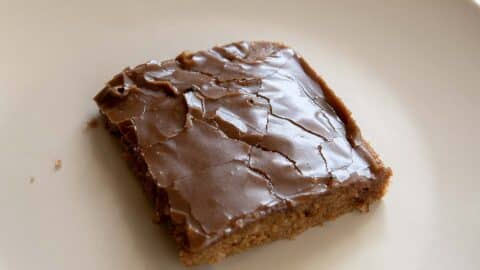 A single square piece of Texas Sheet Cake brownie with a cracked, shiny top sits on a plain white plate.