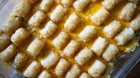 A close-up view of a Tater Tot Hotdish shows rows of golden-brown tater tots over melted cheddar cheese in a clear baking dish.