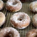 Several sugar-coated donuts are arranged on a wire cooling rack. The donuts have a golden-brown color and a dusting of granulated sugar, perfect for anyone craving a classic treat or searching for the best Baked Apple Cider Donuts Recipe.