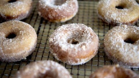 Several sugar-coated donuts are arranged on a wire cooling rack. The donuts have a golden-brown color and a dusting of granulated sugar, perfect for anyone craving a classic treat or searching for the best Baked Apple Cider Donuts Recipe.
