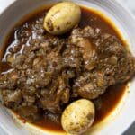 A bowl of Nigerian chicken stew, inspired by Rooster Doro Wat, with two boiled eggs, tender chicken pieces, and chopped onions in a rich, red tomato-based sauce.