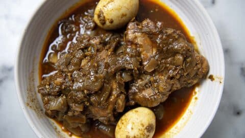 A bowl of Nigerian chicken stew, inspired by Rooster Doro Wat, with two boiled eggs, tender chicken pieces, and chopped onions in a rich, red tomato-based sauce.