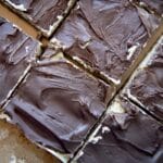 Close-up of Nanaimo Bars cut into squares, revealing a layer of creamy filling beneath a smooth chocolate topping on a parchment-lined surface.
