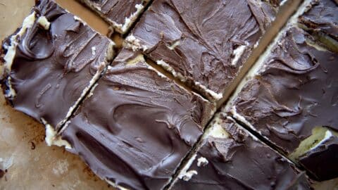 Close-up of Nanaimo Bars cut into squares, revealing a layer of creamy filling beneath a smooth chocolate topping on a parchment-lined surface.