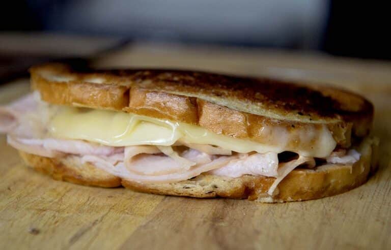 A close-up of a Turkey Reuben toasted sandwich with melted cheese and sliced turkey on golden brown bread, resting on a wooden surface.