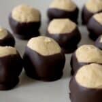 Several buckeye candies, made with the Easy Buckeyes Recipe, feature creamy peanut butter centers partially dipped in chocolate and are arranged on a light-colored plate.
